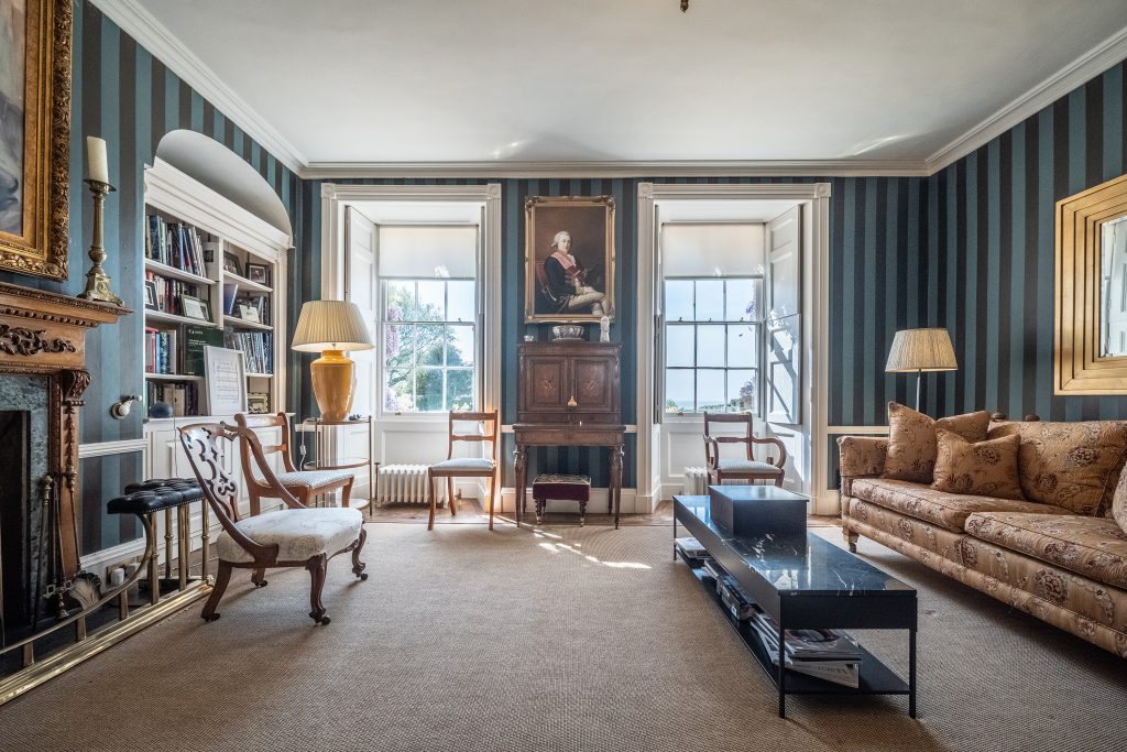 Period drawing room with striped walls, antique furniture and tall sash windows